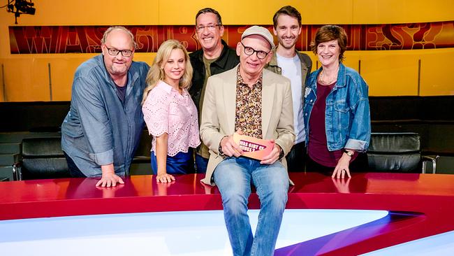 Günther Lainer, Katharina Straßer, Viktor Gernot, Oliver Baier, Clemens Maria Schreiner und Michaela Obertscheider posieren lächelnd im farbenfrohen Studio der Sendung „Was gibt es Neues?“ vor dem roten Pult.
