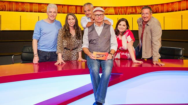Michael Mittermeier, Lydia Prenner-Kasper, Thomas Maurer, Isabell Pannagl und Viktor Gernot posieren lächelnd um einen farbenfrohen "Was gibt es Neues?"-Studiotisch, während Oliver Baier in Weste und Kappe vorne sitzt und Moderationskarten hält.