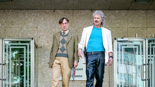 Roland Düringer und Alfred Dorfer stehen vor einem Amtsgebäude