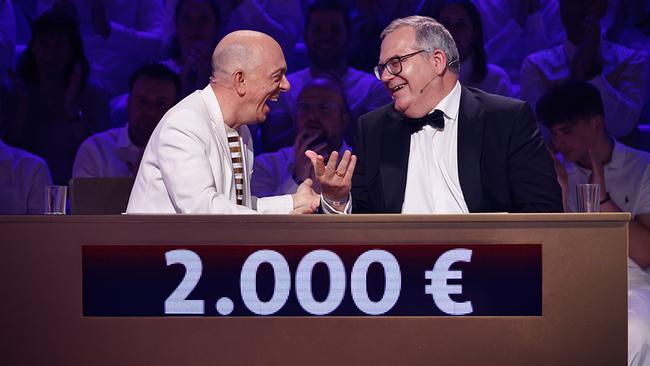 Bernhard Hoëcker und Elton, beide elegant gekleidet, sitzen sich freuend hinter dem Spielepult "Wer weiß denn sowas XXL" vor einem Display, das einen Gewinn von 2.000 Euro anzeigt.