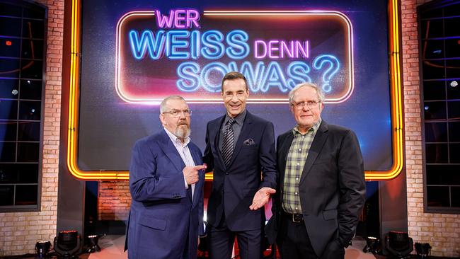 © ORF/NDR/Morris Mac Matzen Dietmar Bär, Kai Pflaume und Harald Krassnitzer stehen nebeneinander im Fernsehstudio vor dem leuchtenden Logo der Quizshow "Wer weiß denn sowas?".