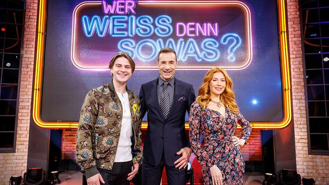 © ORF/NDR/Morris Mac Matzen Moderator Kai Pflaume steht mit Palina Rojinski und Vincent Gross im Fernsehstudio vor dem leuchtenden Logo der Quizshow "Wer weiß denn sowas?".