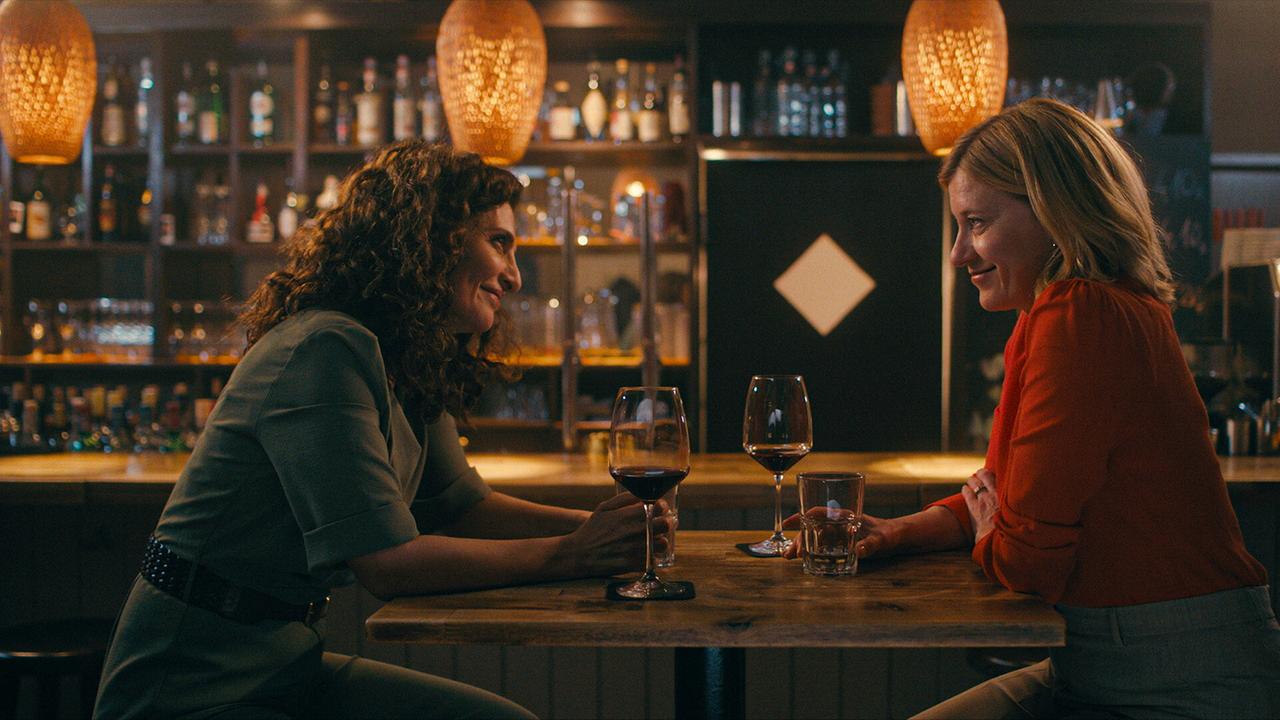 © ORF/Praherfilm/Nikolaus Geyrhalter Filmproduktion Fa und Marie Theres sitzen sich an einem Holztisch in einer Bar gegenüber und trinken ein Glas Rotwein.