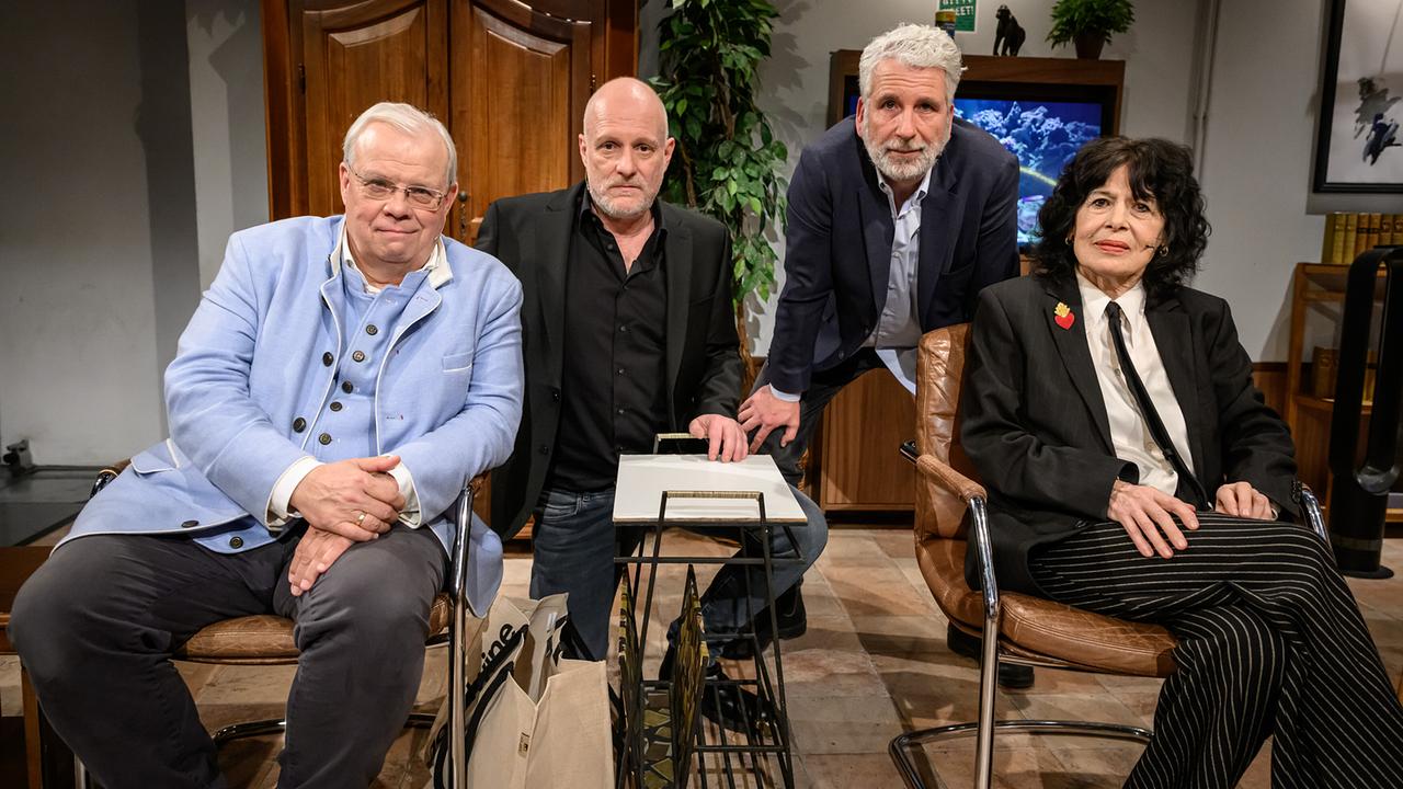 Christian Wehrschütz, Christoph Grissemann, Dirk Stermann und Monika Helfer nebeneinander beim Gruppenfoto im "Willkommen Österreich"-Studio vor einem Aquarium.