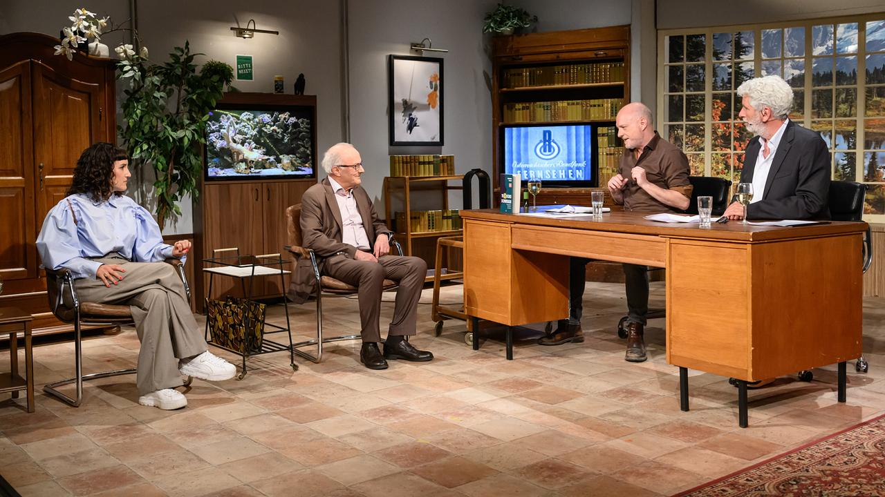 © ORF/Hans Leitner In einem gemütlich eingerichteten "Willkommen Österreich"-Studio sitzen Ina Regen und Reinhard Haller auf Sesseln und führen ein Gespräch mit Christoph Grissemann und Dirk Stermann, die an einem Holzschreibtisch sitzen.
