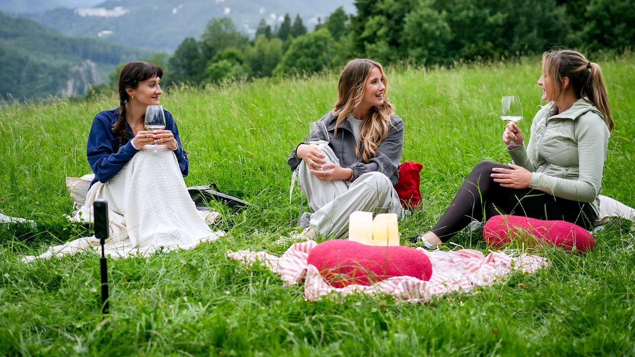 © ORF/TVfriends Moderatorin Michelle Pippan und die Kandidatinnen Susanna und Sarah sitzen mit einem Glas Wein auf einer Wiese