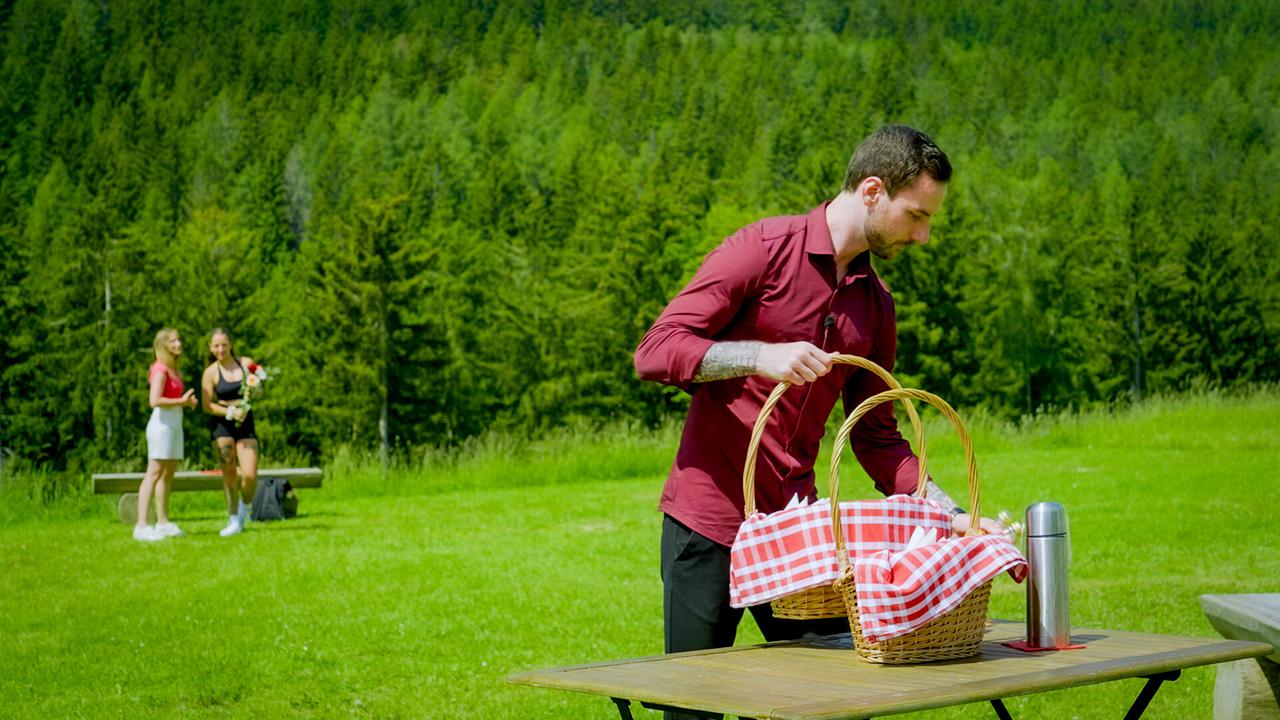 Kandidat Richard muss auf einer Wiese aus zwei Picknickkörben wählen, während Date Sophie und Michelle Pippan im Hintergrund warten.