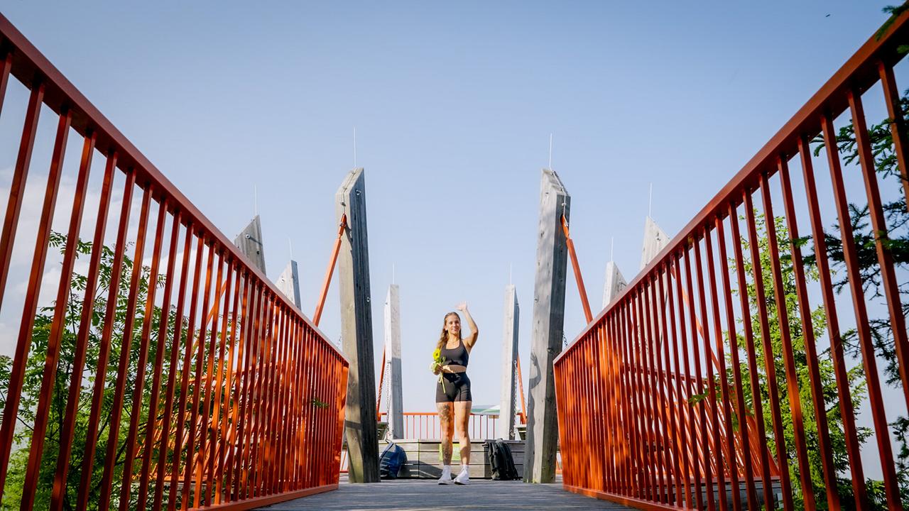 Sophie steht mit einer Sonnenblume auf einer roten Brücke.