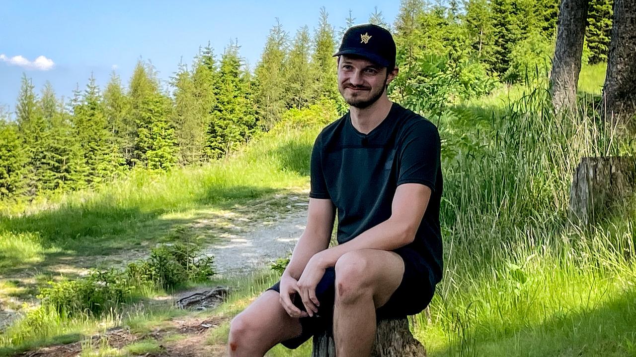 Kandidat Michael sitzt auf einem Baumstumpf inmitten einer grünen Waldlandschaft.
