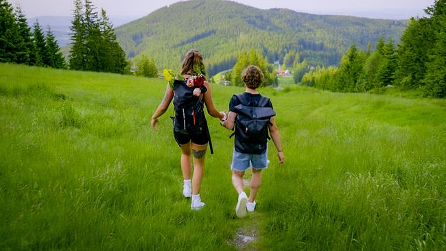 © ORF/TVfriends Single Sophie und Kandidat Ferdinand halten sich die Hände beim Gehen über eine grüne Wiese mit Bergblick.