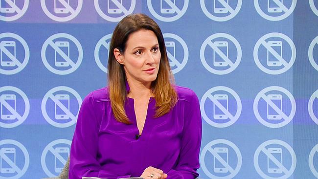 Lisa Gadenstätter sitzt im Fernsehstudio vor einem Hintergrund mit wiederholten Smartphone‑Symbolen, die durchgestrichen sind.