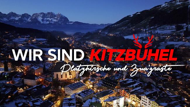 © ORF/west4media Eine nächtliche Winteraufnahme zeigt Kitzbühel, dessen beleuchtete Häuser sich unter dem Slogan "Wir sind Kitzbühel - Platzhirsche und Zua'graste" erstrecken.
