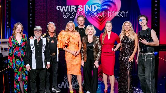 Zoë Straub, Thomas Forstner, Waterloo, Barbara Schöneberger, Lucas Fendrich, Elisabeth Engstler, Nina Proll, Simone und COSMÓ gemeinsam auf einer glänzenden Bühne vor dem Schriftzug „WIR SIND SONG CONTEST“.