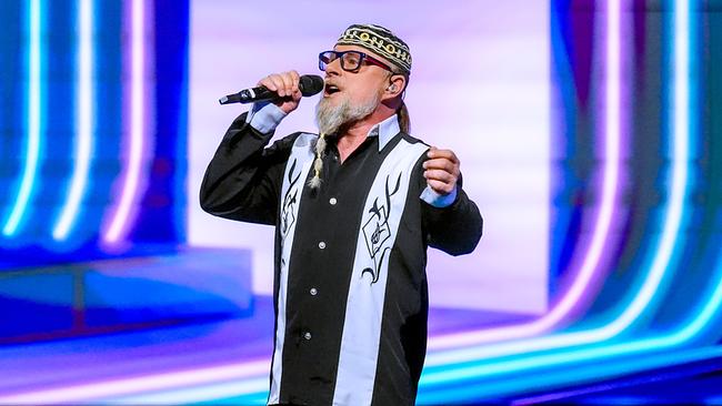 © ORF/Roman Zach-Kiesling Thomas Forstner singt auf einer hell beleuchteten Bühne in ein Mikrofon und trägt ein schwarz-weißes Hemd sowie eine auffällige Kopfbedeckung.