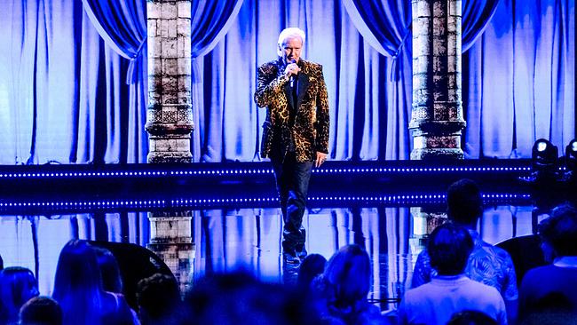 Johnny Logan auf einer hell beleuchteten Bühne singt mit einem Mikrofon zu einem Publikum.