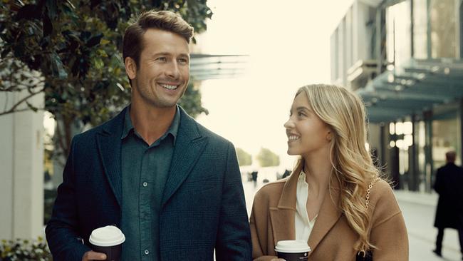 Ein Mann und eine Frau gehen nebeneinander eine Straße entlang, beide halten einn Coffee-to-Go-Becher in der Hand und lächeln freundlich