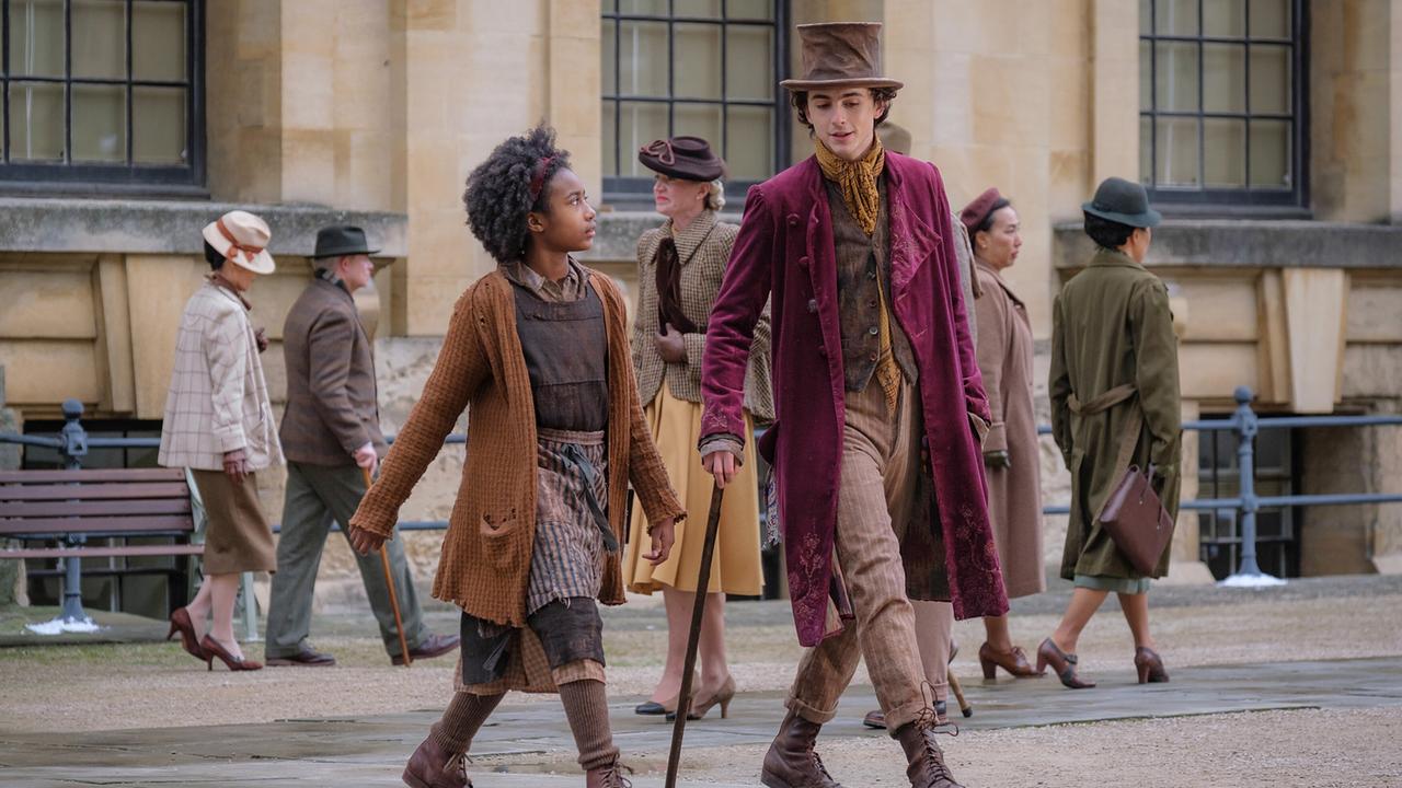 Willy Wonka mit braunem Zylinder und langem Mantel, Noodle in braunem Strickcardigan; im Hintergrund weitere Passanten in historischer Kleidung