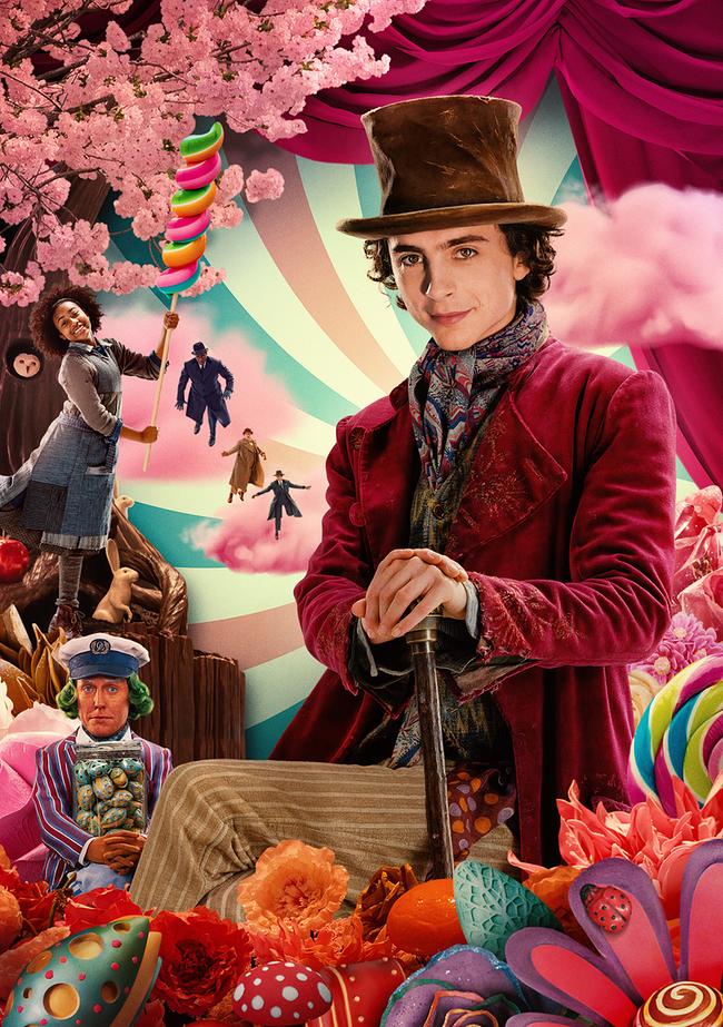 Ein Mann im roten Samtmantel und braunem Zylinder sitzt mit Gehstock in einer farbenfrohen Fantasiewelt voller Süßigkeiten, Blumen und verspielten Figuren