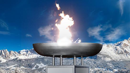 Eine olympische Flamme brennt bei Tag vor einer Bergkulisse.