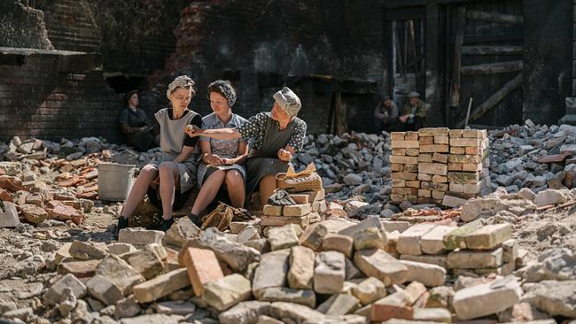 Drei Frauen machen Pause auf einem Trümmerhaufen.