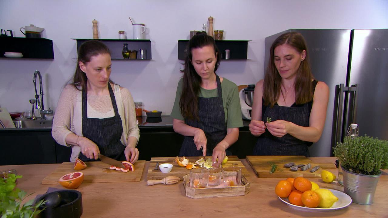Drei Frauen bereiten Gerichte aus Zitrusfrüchten in einer modernen Küche zu