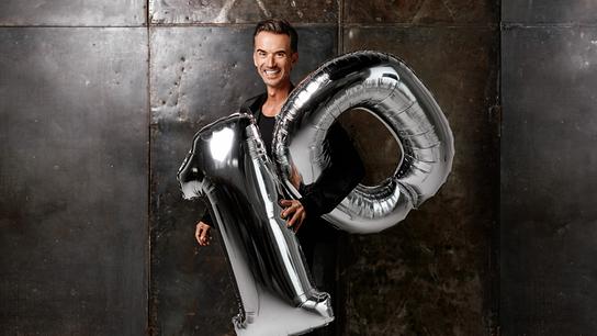 Florian Silbereisen präsentiert "10 Jahre Schlagerbooom" und hält vor einer dunklen Wand große silberne Folienballons in Form der Zahl 10.