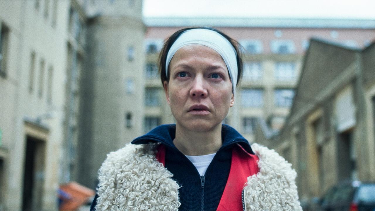 Jenny von Loeben steht frontal in einem Hof zwischen Gebäuden und blickt nach vorne.