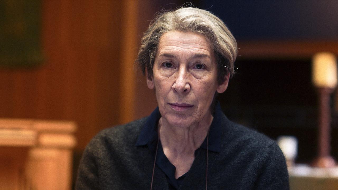 Frau Markowski sitzt in einem Gerichtssaal mit warmem Licht und unscharfem Hintergrund und blickt nach vorne.