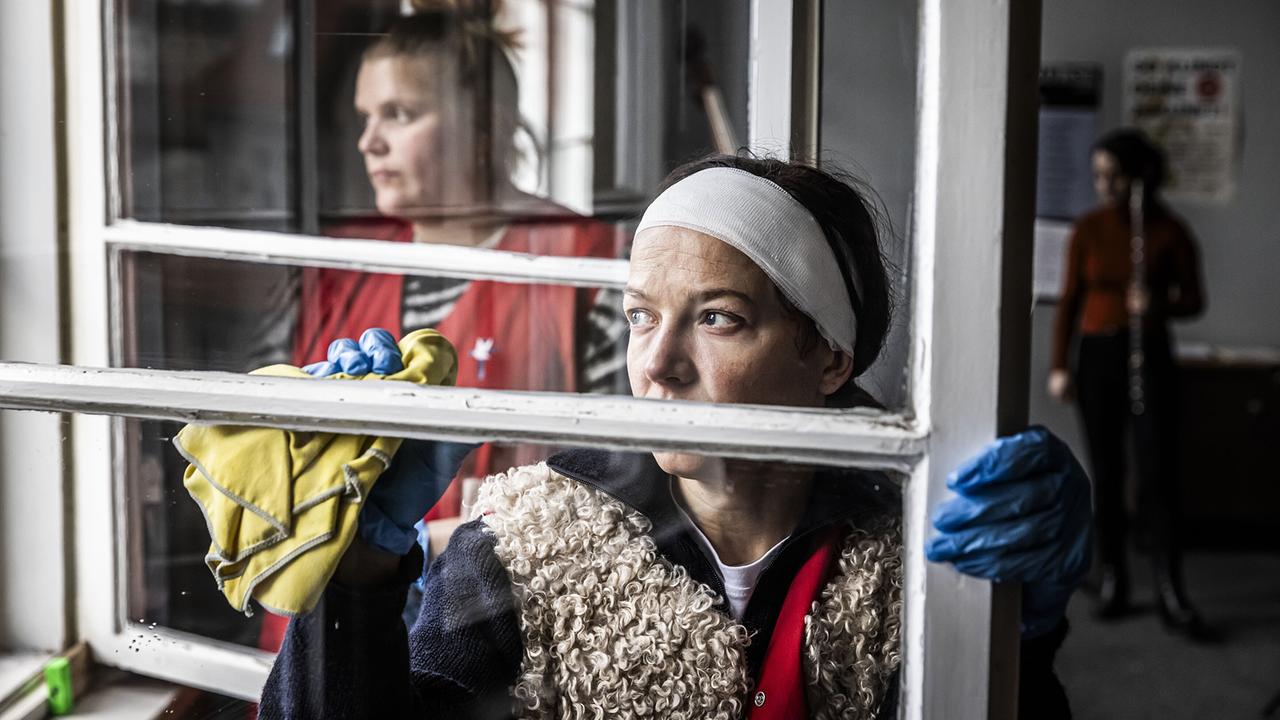 Jenny von Loeben reinigt mit Handschuhen ein Fenster, während im Hintergrund weiteres Reinigungspersonal zu sehen ist.