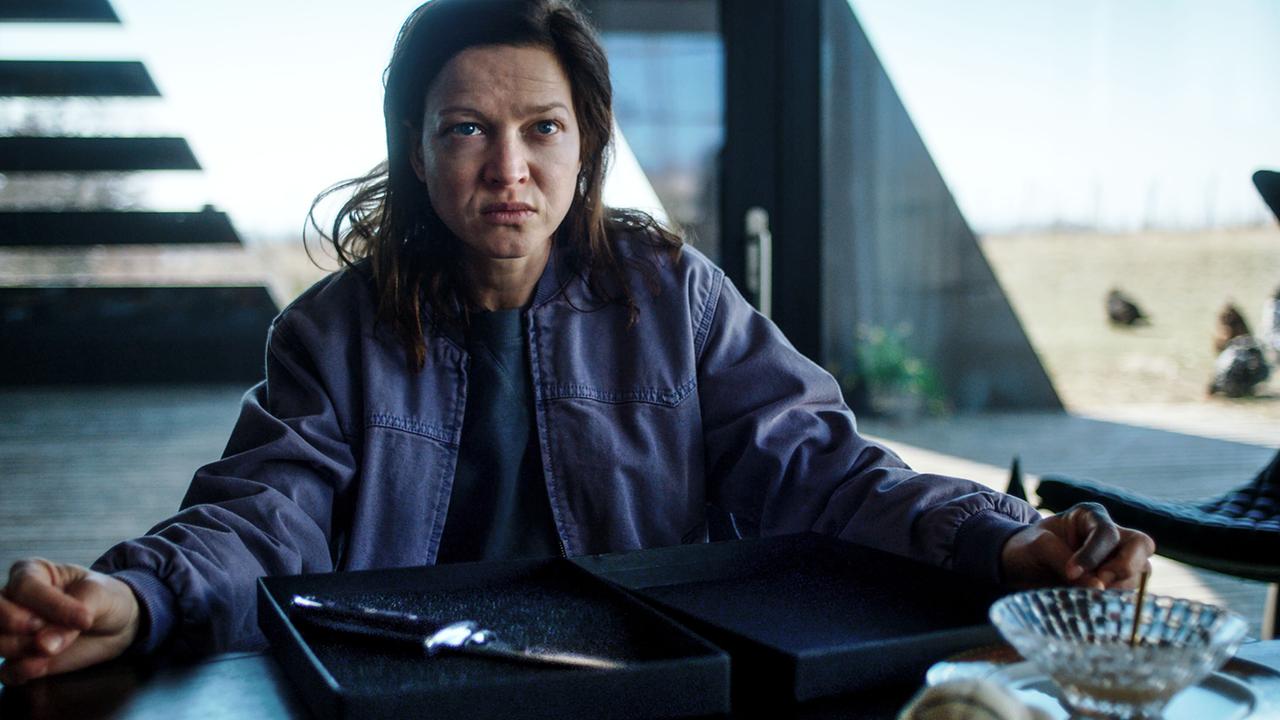 Jenny von Loeben  sitzt an einem Tisch vor geöffneten Schachteln in einem modernen Raum vor einer Fensterfront.