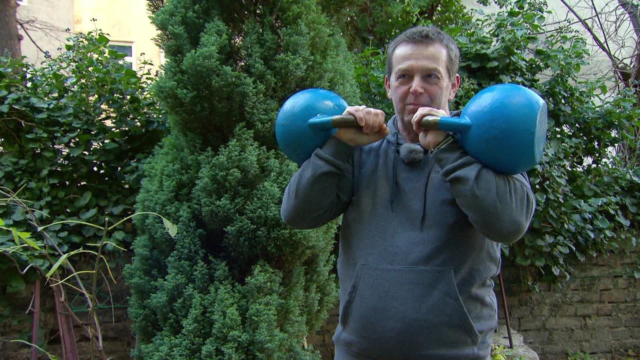 Mann steht im Garten und trainiert mit Kettlebells 