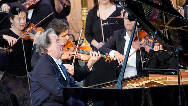 Rudolf Buchbinder spielt am Klavier, im Hintergrund spielen Streicher.
