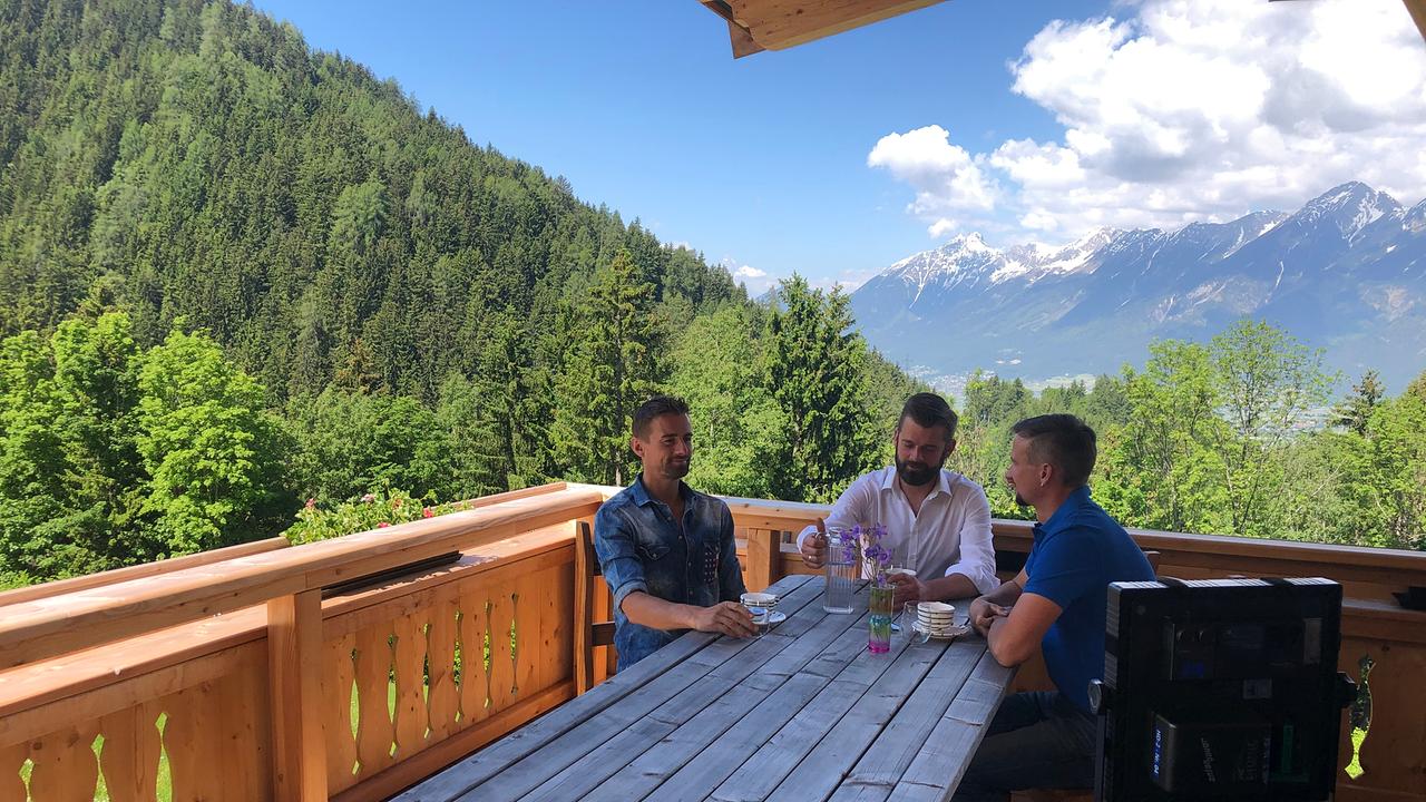 Die Grubertaler sitzen gemeinsam an einem Tisch auf einer Terrasse mit Bergpanorama im Hintergrund