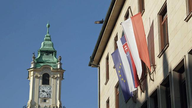 Kirchturm neben Haus mit Fahnen der EU, der Slowakei und Bratislavas