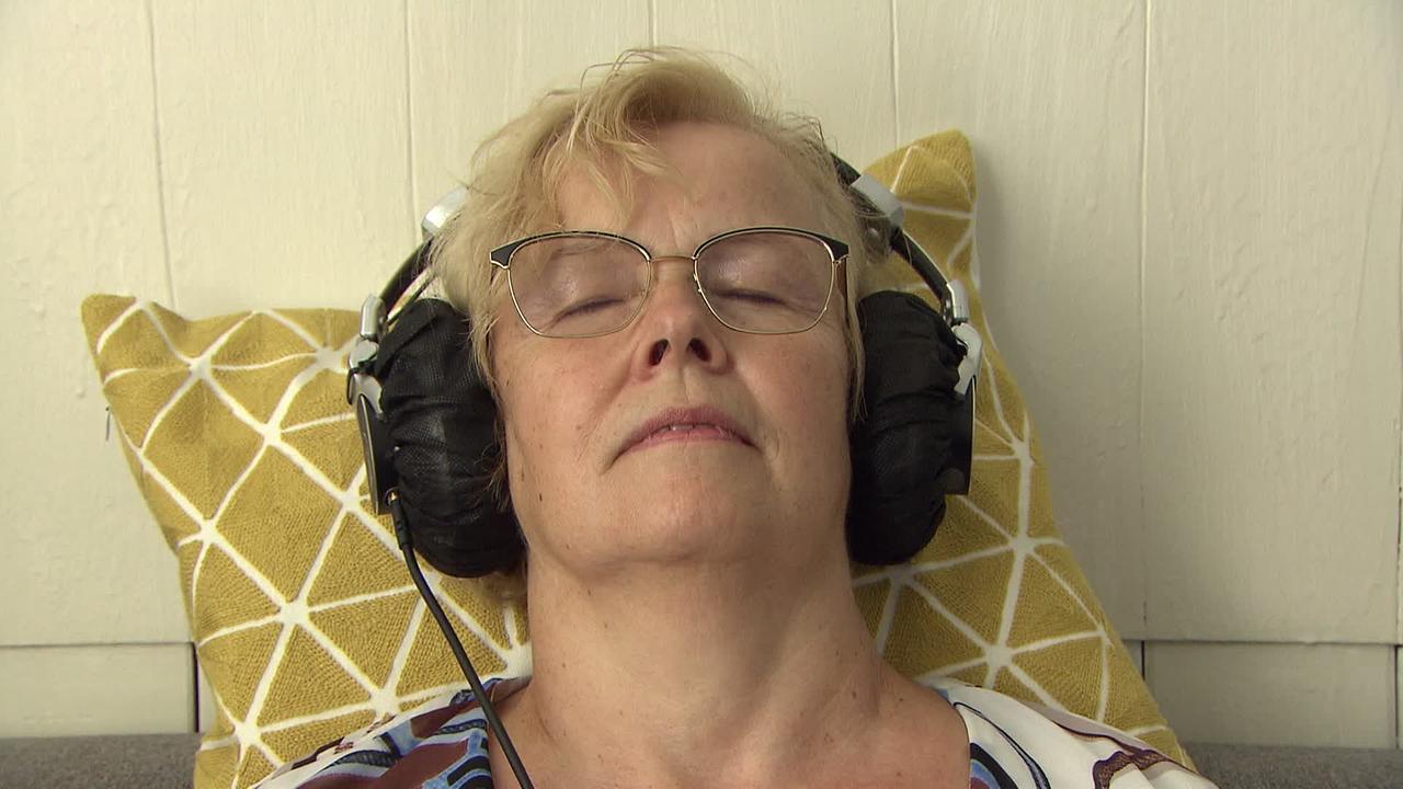 Ältere Frau liegt in Praxis und hat Kopfhörer auf