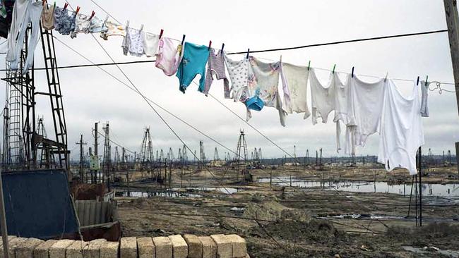 Eine Wäscheleine voller Kinderkleidung, im Hintergrund Ölförderstellen und verwüstete Landschaft in Baku/Aserbeidschan (Liquid Land, 2008; Künstlerin: Rena Effendi)