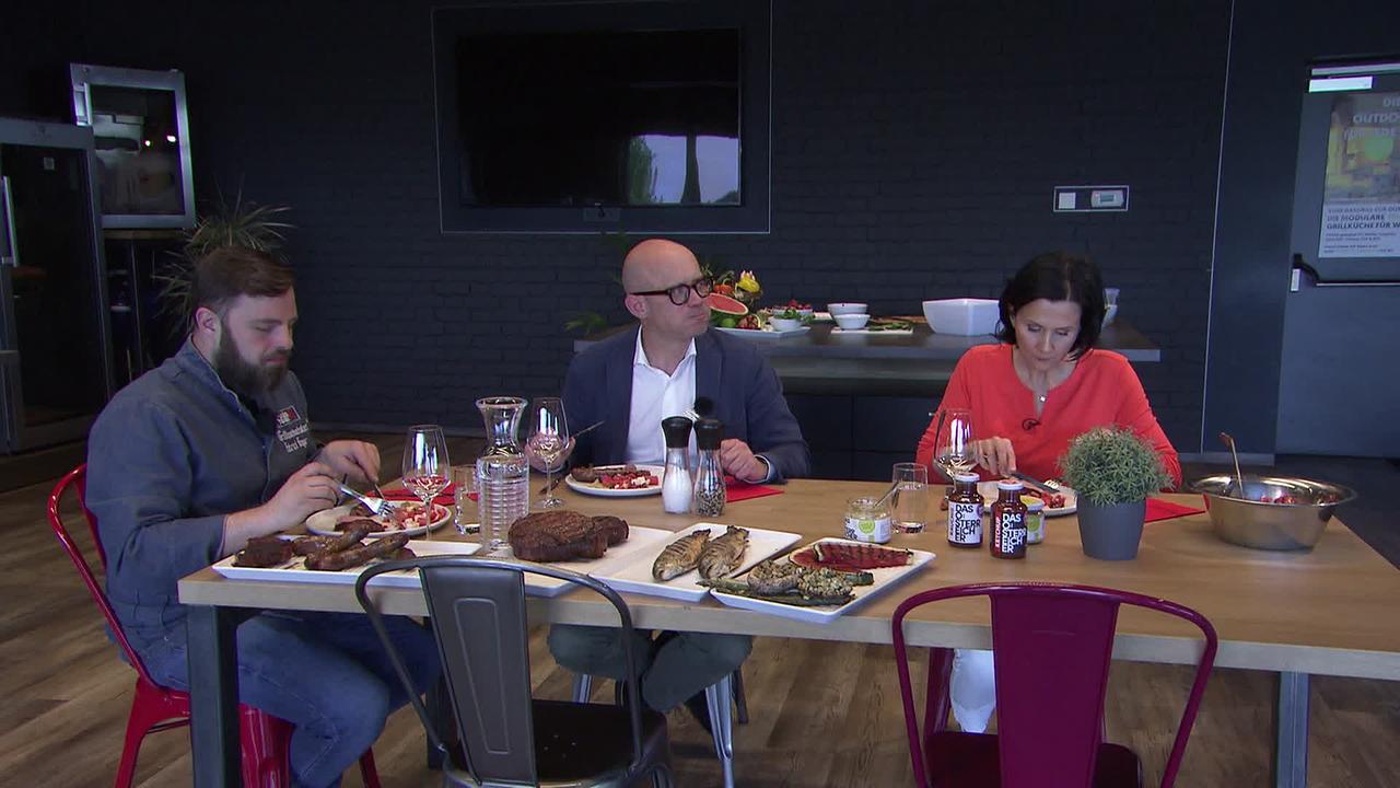 Drei Personen sitzen am Tisch und essen gegrillte Speisen