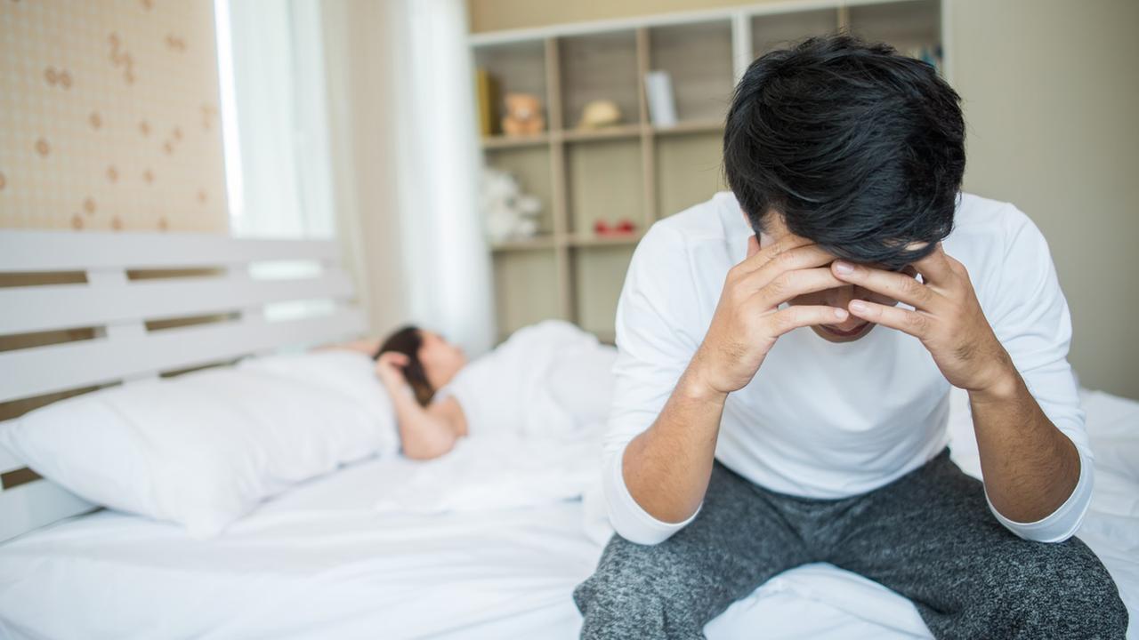 © Bild von jcomp auf Freepik Mann sitzt mit in die Hände gestützem Kopf am Bettrand, im Hintergrund liegt eine Frau im Bett.