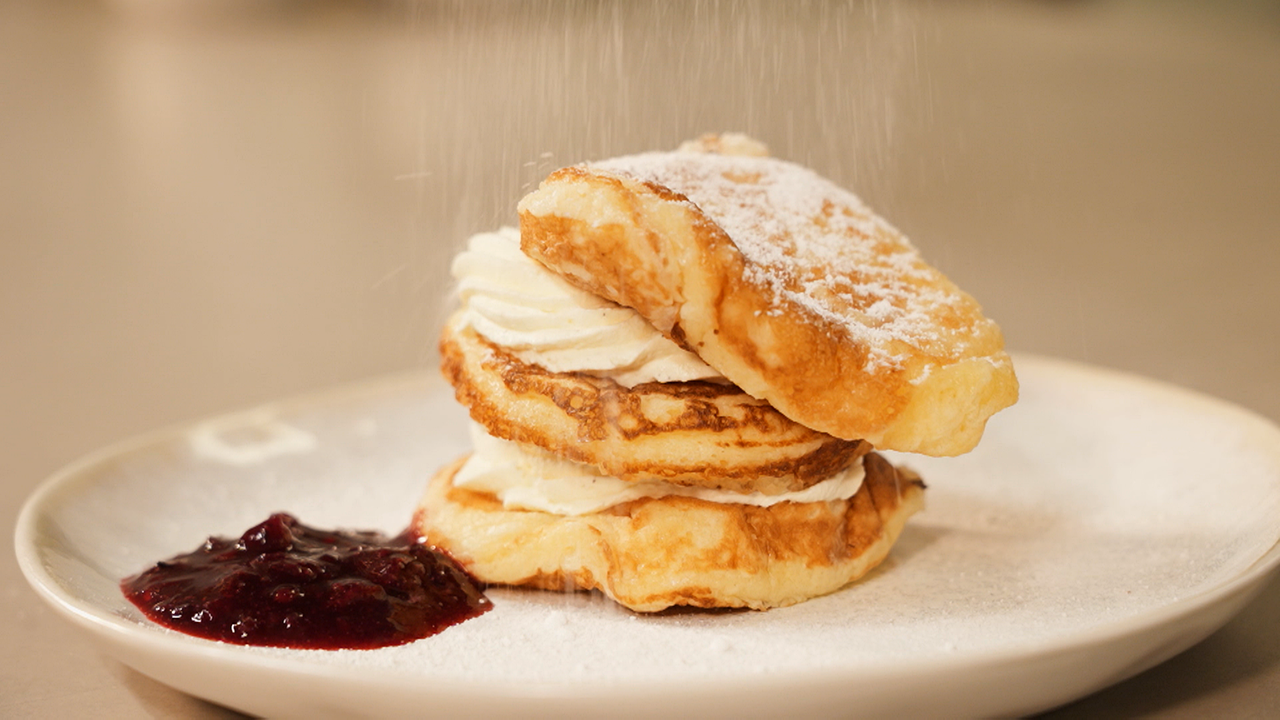 Drei kleine Pfannkuchen liegen übereinander und werden mit Zucker bestreut