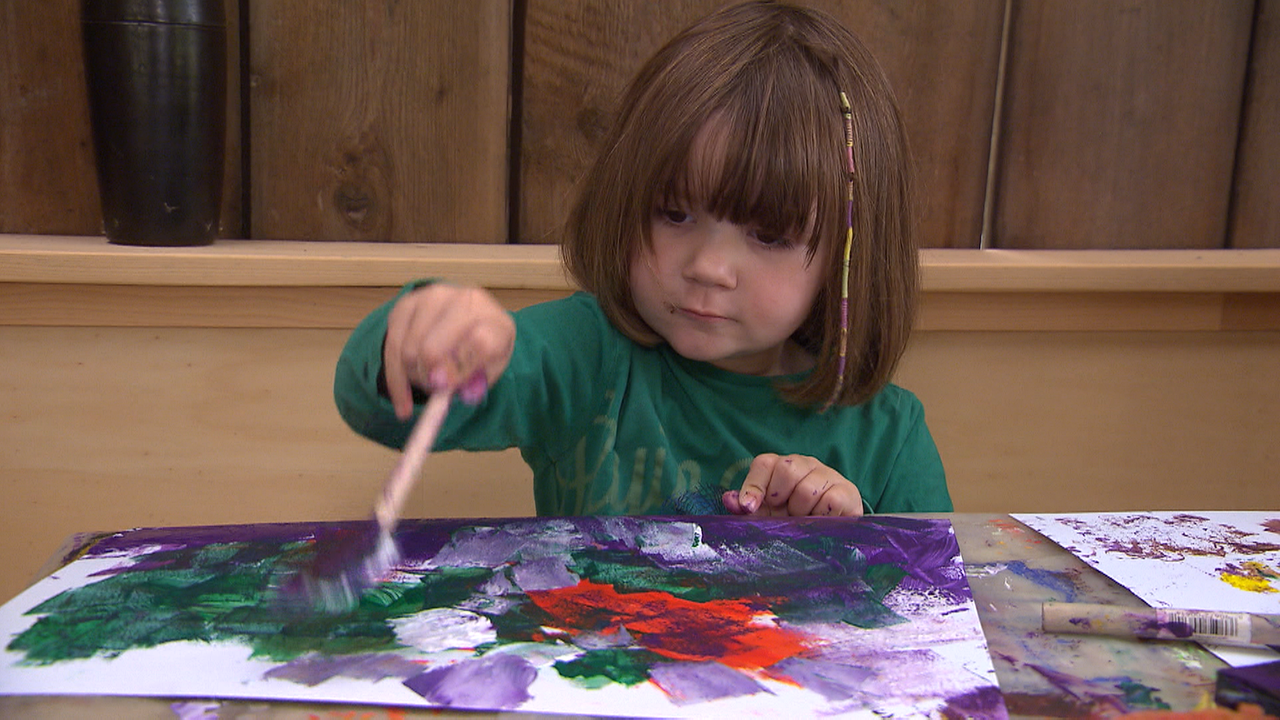 Ein kleines Kind sitzt und malt ein buntes Bild mit dem Pinsel.