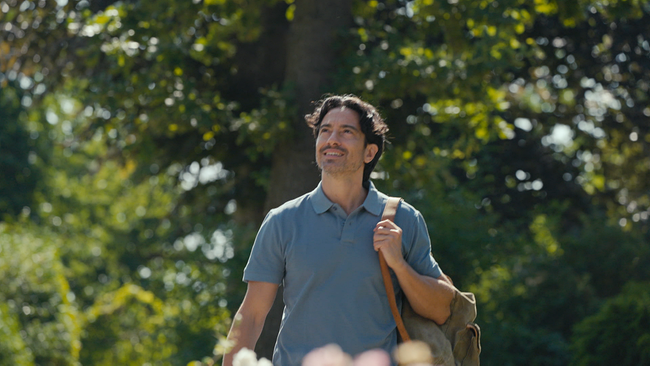Schauspieler Stefano Bernardin wandert - mit einem Rücksack über eine Schulter gehängt - durch einen lichten Wald
