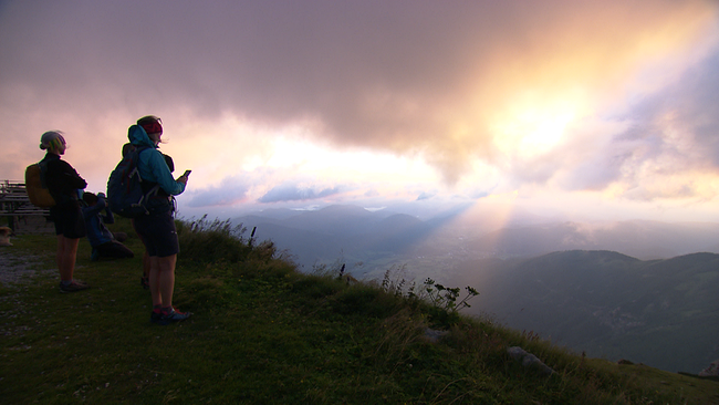 Wanderer blicken vom Berg ins Tal Richtung Sonnenaufgang