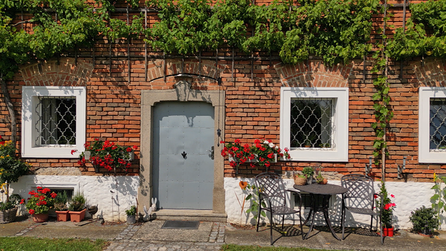 Eingangsbereich eines Vierkanters von außen, mit roten Blumen dekoriert, Ziegelmauer