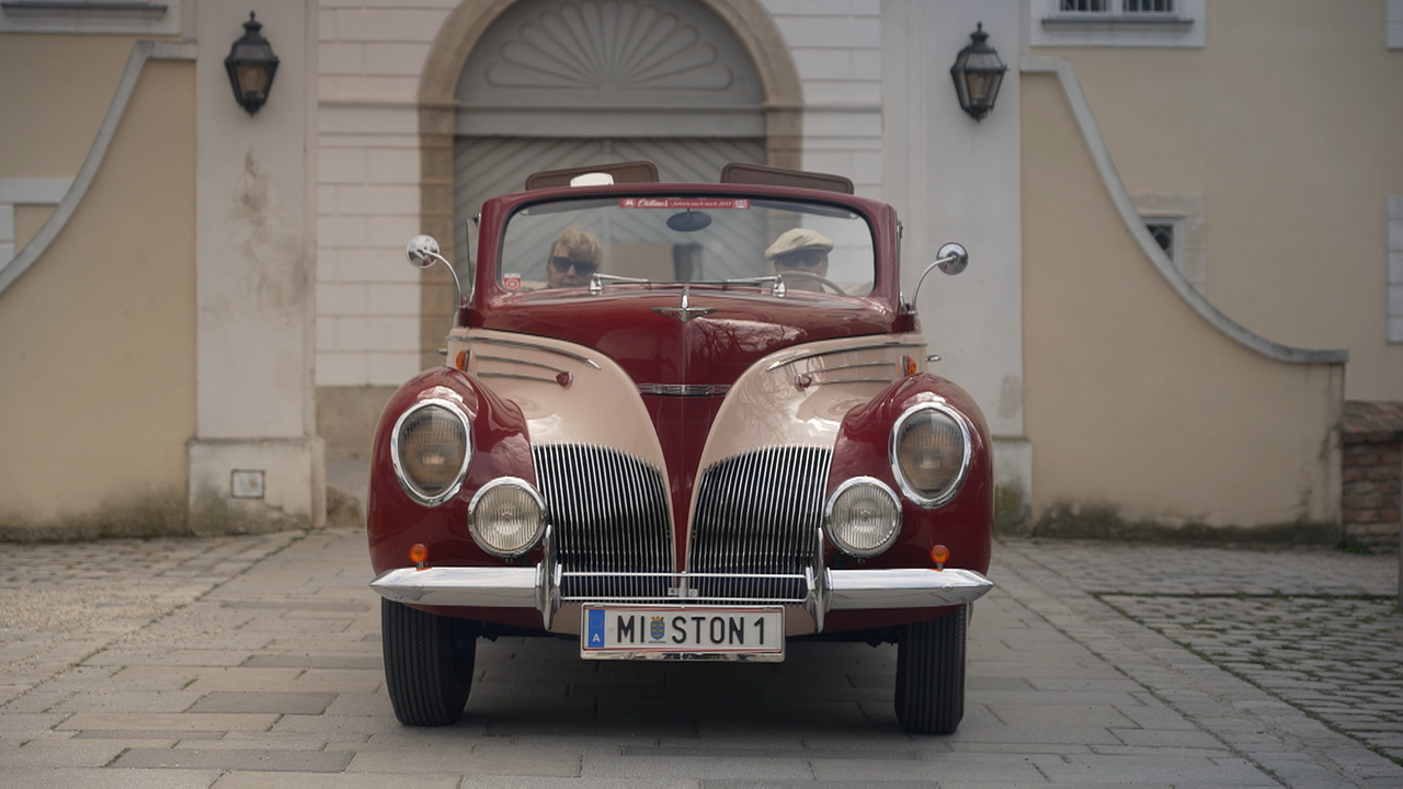 rot-beiger Oldtimer steht vor einem Schlosstor