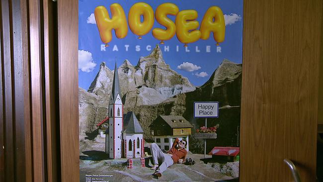 Hosea Ratschiller entspannt in Ortskulisse liegend. Plakat zu seinem Programm "Happy Place".