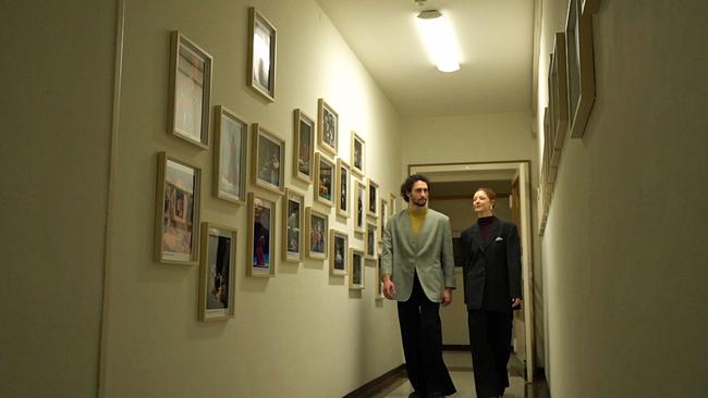 © ORF Alessandro Frola und Madison Young gehen in Staatsoper Garderobengang mit Fotos von TänzerInnen entlang.