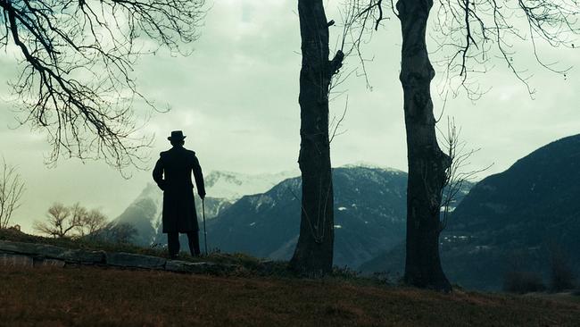 Schwarze Silhouette von Mann mit Hut und Stock schaut in gebirgige Landschaft