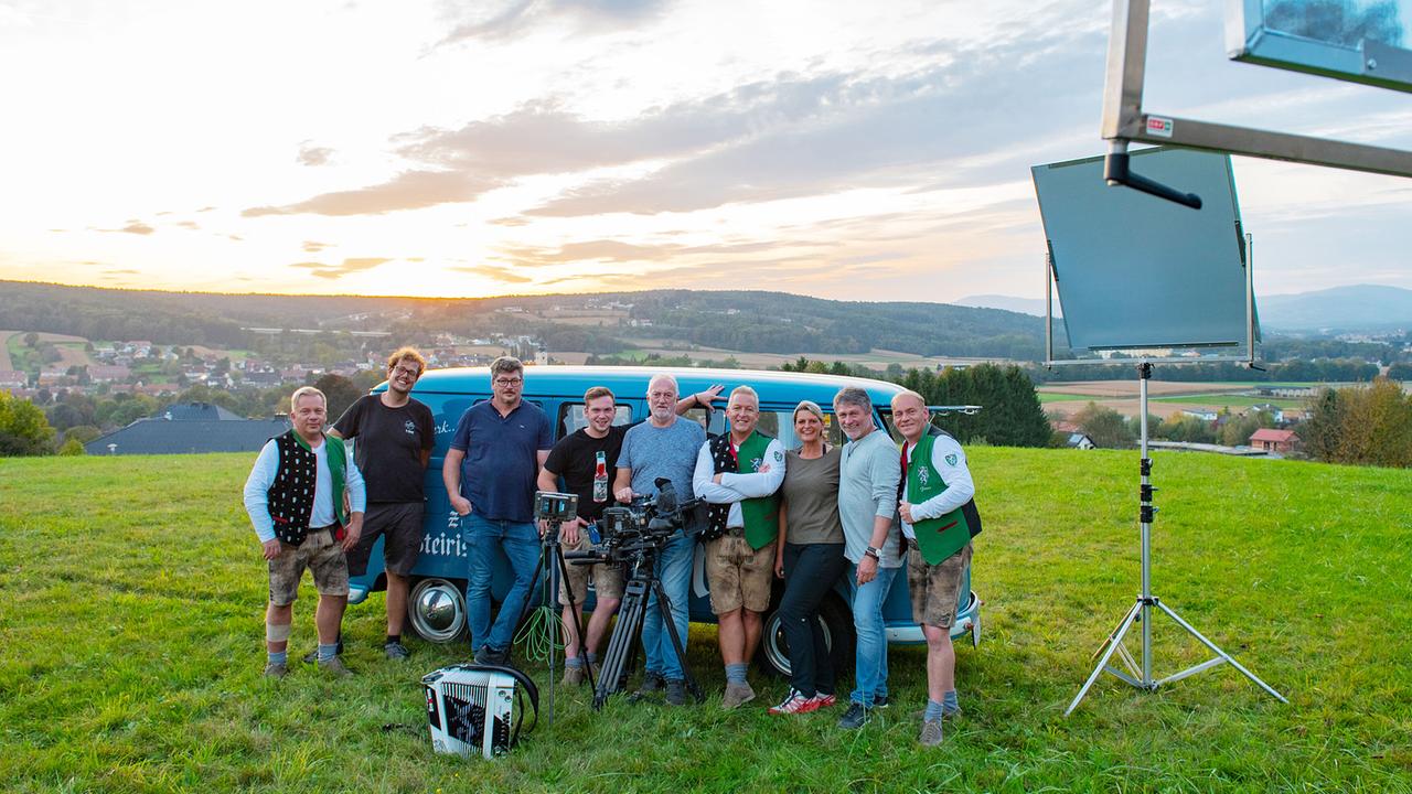 "Die Edlseer" stehen gemeinsam mit dem Filmteam vor „Bulli“, dem alten Tourbus, auf einer Wiese bei Sonnenuntergang, umgeben von Kameraequipment.