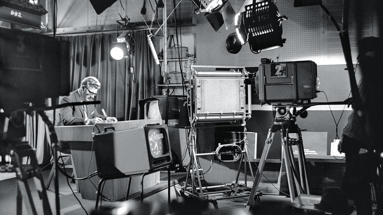 Peter Fichna sitzt 1967 konzentriert am Nachrichtentisch kurz vor dem Beginn der "Zeit im Bild" im Fernsehstudio, , umgeben von Kameras und Technik.