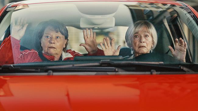 Toni und Helene sitzen mit erhobenen Händen auf den Vordersitzen in einem roten Auto.